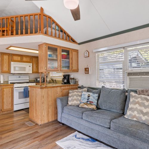 Standing back, this view showcases the airy, open-concept layout with the living area, cozy couch, loft above, and kitchen all in one inviting space.