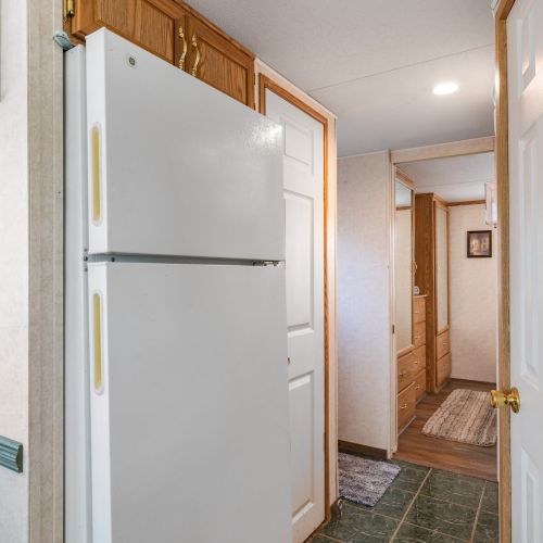 View of the fridge, hallway, and cozy bedroom at the end.