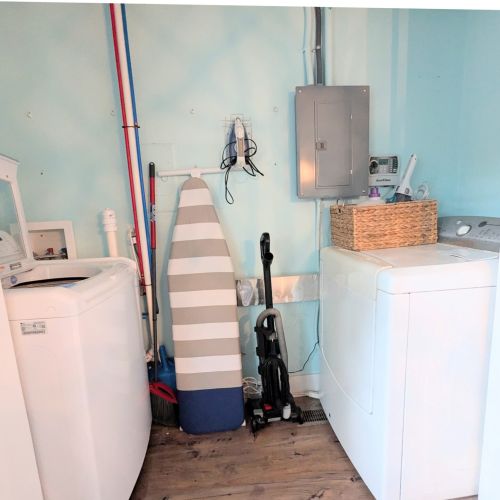 Fully equipped laundry room with washer, dryer, iron, ironing board, vacuum, and broom.