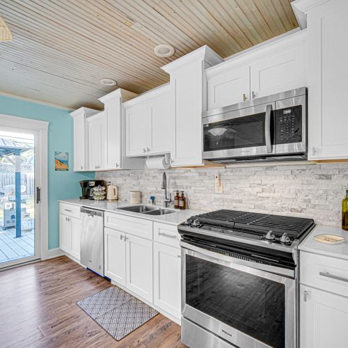 Fully stocked modern kitchen with stainless steel appliances, stone countertops, breakfast bar, and Keurig - everything you need for a beach getaway.
