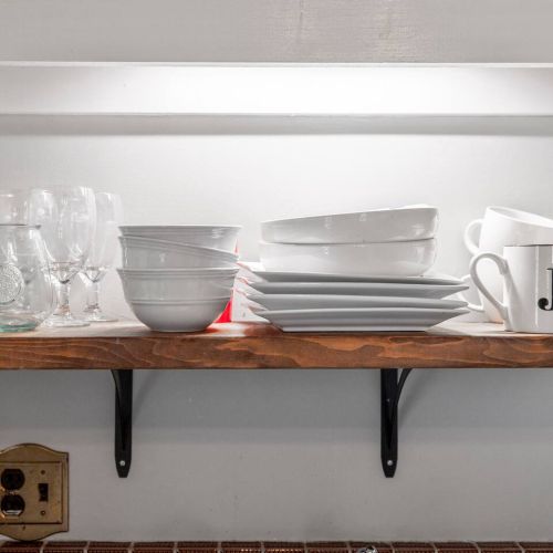 Plates and cups on shelf above kitchen sink.