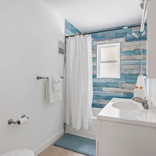 Fresh, bright bathroom featuring white finishes and a charming blue shiplap bathtub/shower area.
