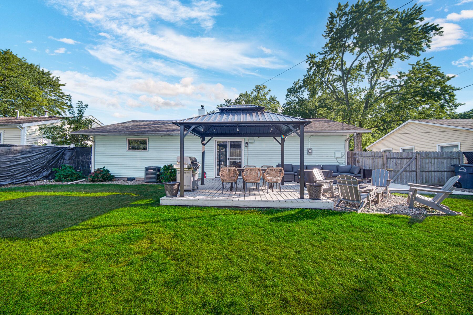 Spacious fenced backyard with deck, Adirondack chairs, and outdoor dining - perfect for grilling, lounging, and making memories under the stars.